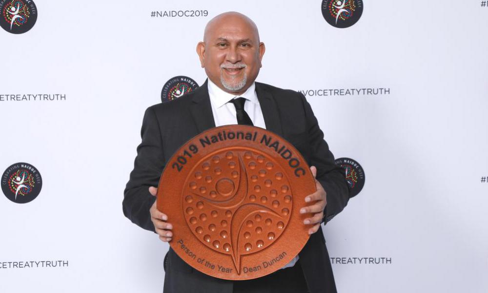 Man stands holding an Award: 2019 National NAIDOC