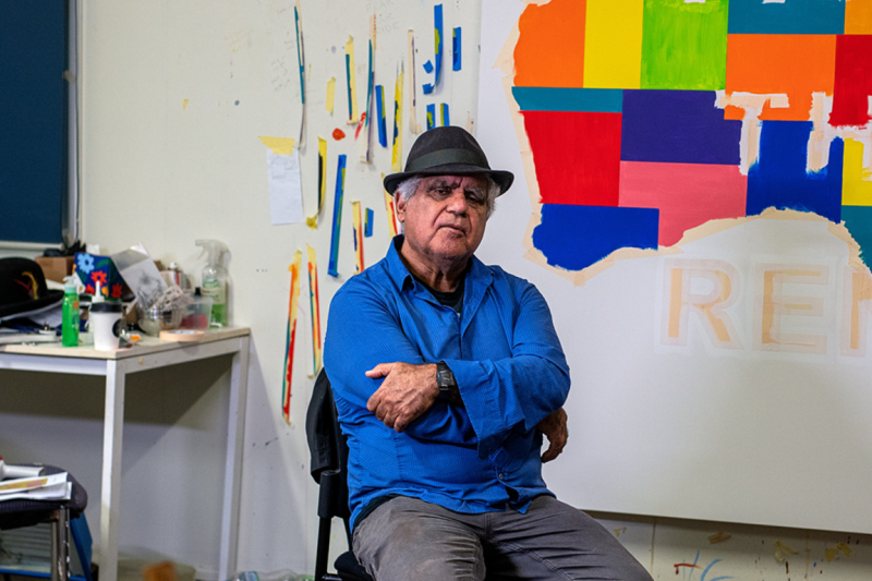 Artist Richard Bell sitting on a chair in his studio.