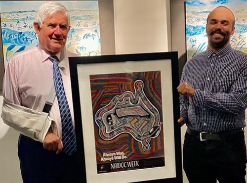 The Hon Ken Wyatt AM MP holding the 2020 NAIDOC Poster with the artist, Tyrown Waigana
