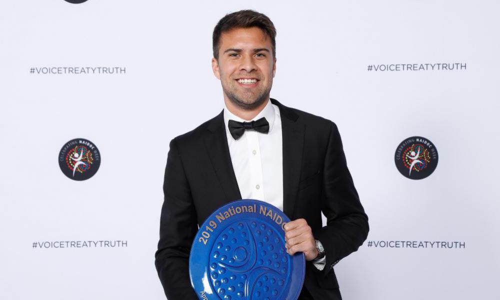 Man stands holding an Award: 2019 National NAIDOC