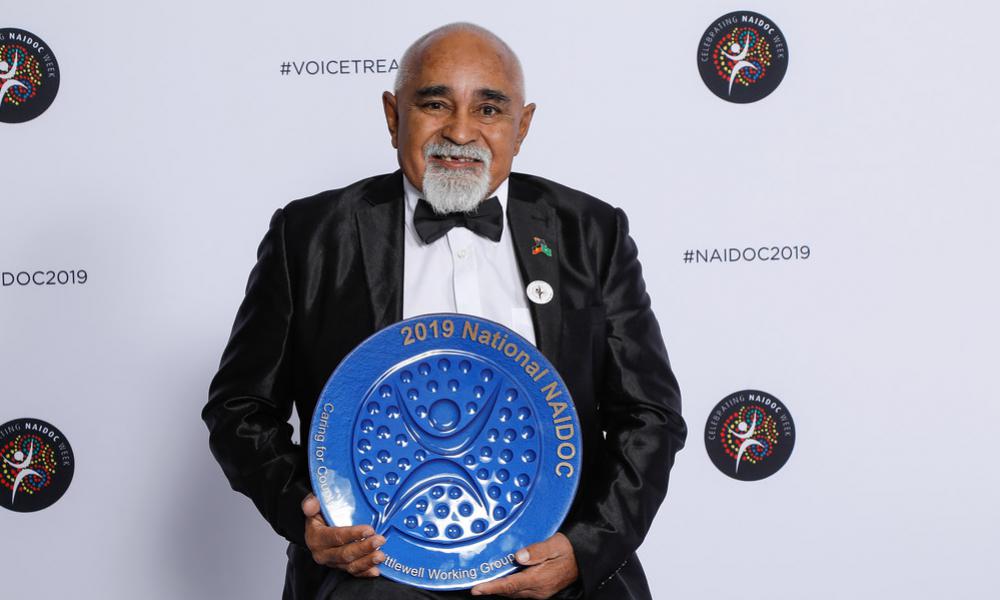 Man stands holding an Award: 2019 National NAIDOC