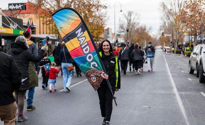 A woman holds a NAIDOC flag in a parade