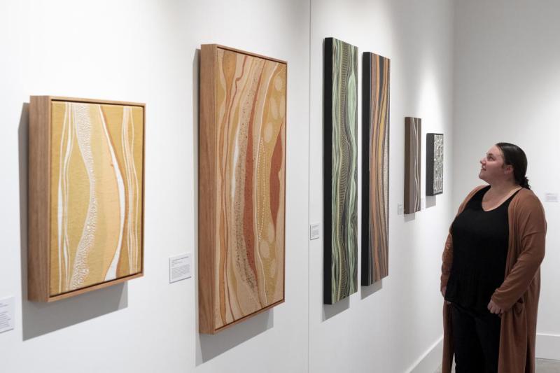 Arakwal Bundjalung artist Nickolla Clark is standing looking at her artworks in the exhibition 'Gabul Jagun – Carpet Snake Country' at Lone Goat Gallery